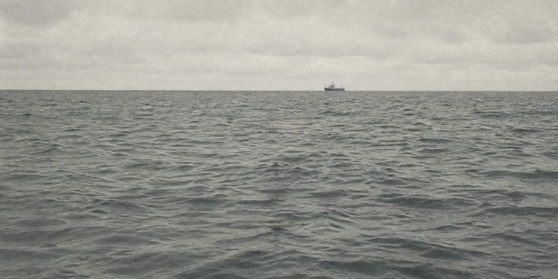 Calm grey-green sea with a small fishing boat under flat overcast light
